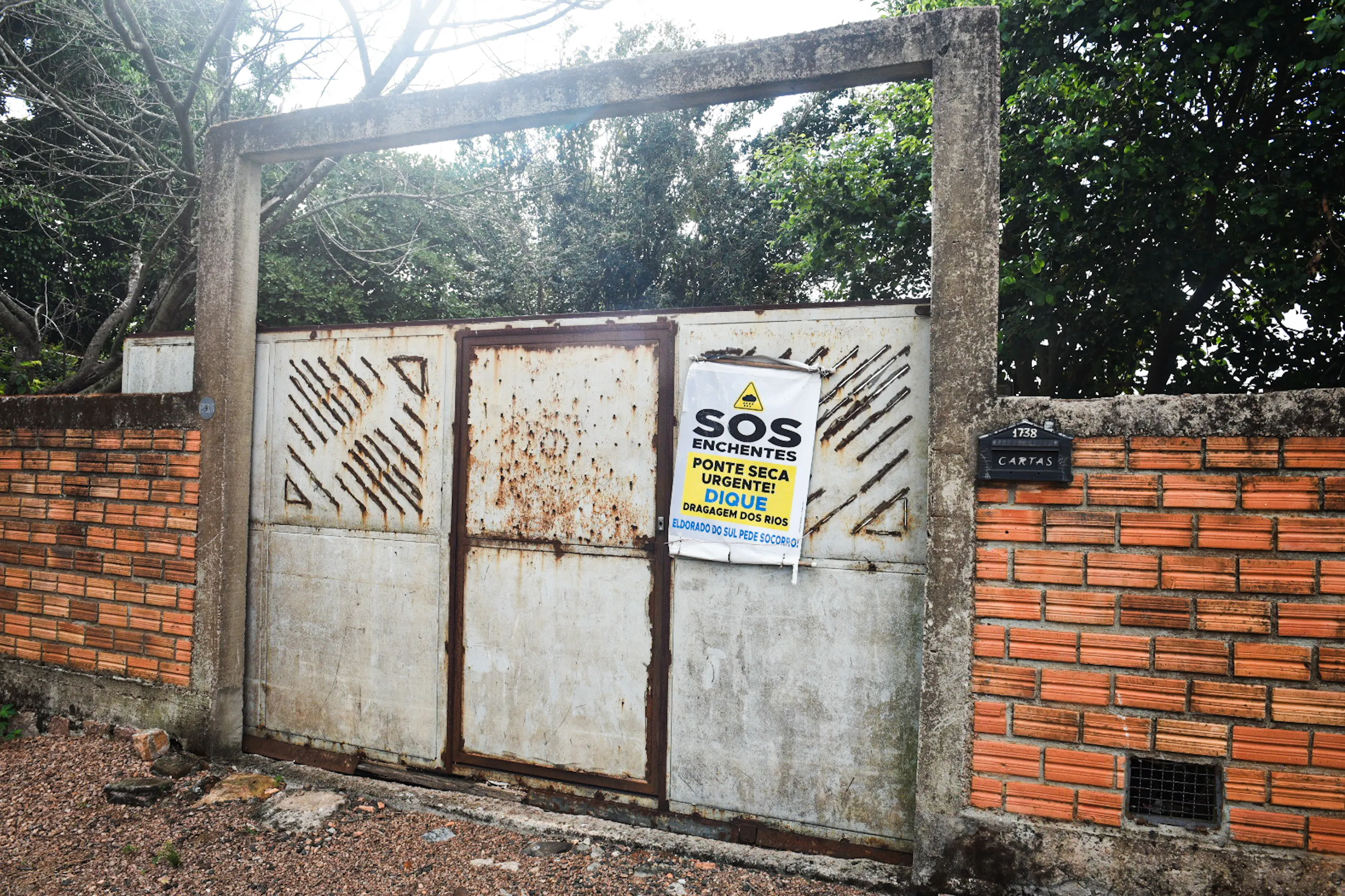 The gate of a flood-damaged home condemned after the severe 2024 floods, bears a poster from a local campaign calling for improved flood-protection measures. Photo by Alass Derivas.