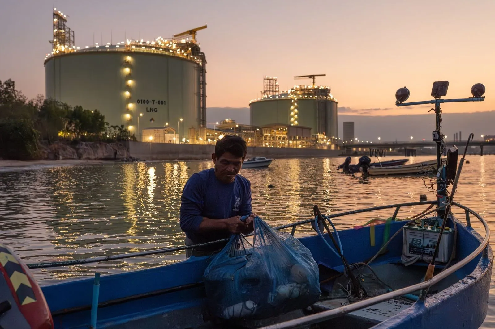 A fisher offloads gear in front of a liquefied natural gas terminal operated by state-owned energy company PTT Public Company Limited at the Map Ta Phut Industrial Port in Rayong province, Thailand, on Feb. 4, 2026. Photo by Andy Ball for Mongabay.