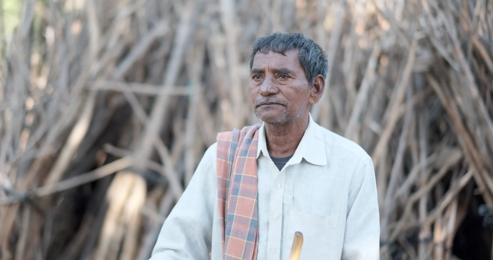Chelluri Narasimha, a Dalit farmer from Tarluvada, stands below Chukka Konda hill. Narasimha's teak plantation has been notified for acquisition for Google's 1 GW data center. Narasimha says the land is his only livelihood and opposes acquisition.